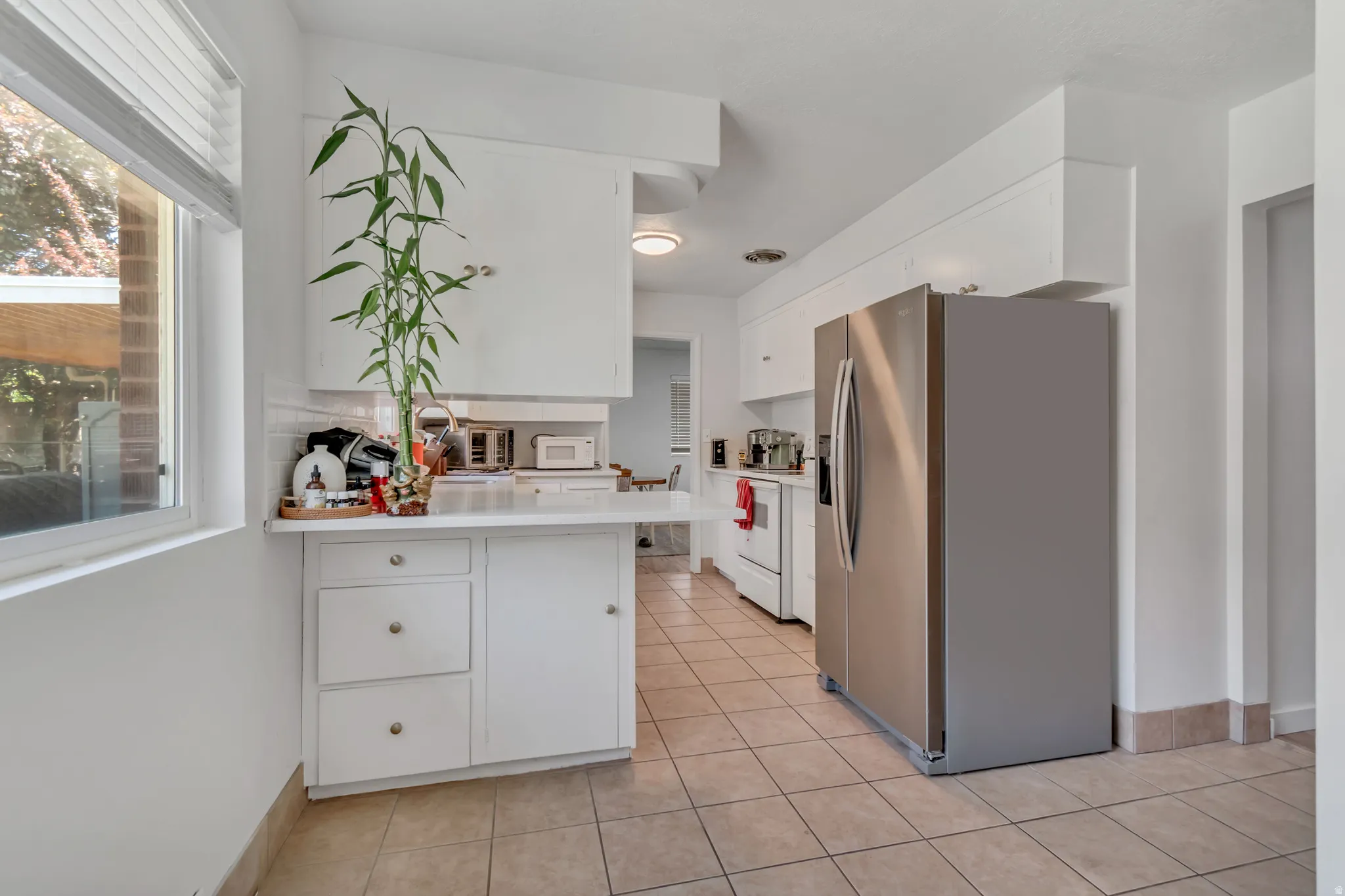 Kitchen featuring stainless steel fridge with ice dispenser, white cabinetry, light countertops, and a peninsula
