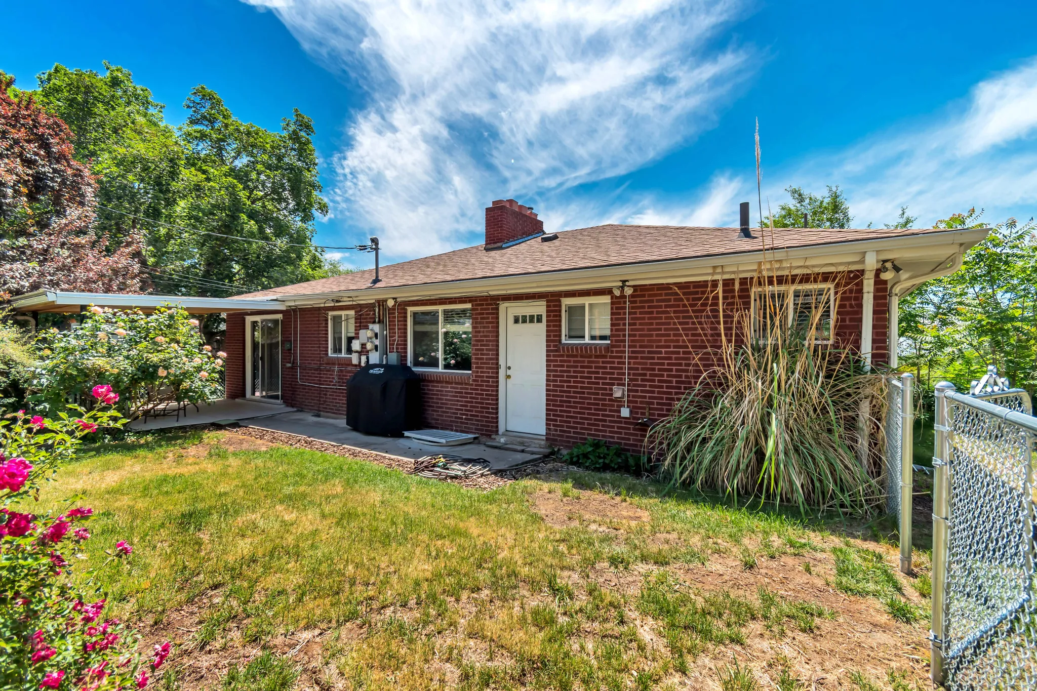 Back of house with brick siding, a chimney, a patio area, and a shingled roof