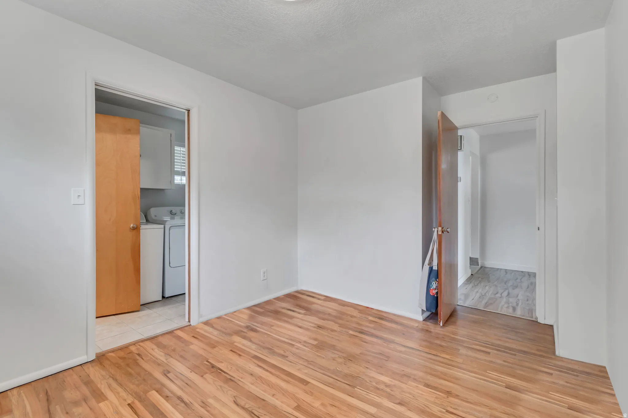 Empty room with light wood-type flooring, a textured ceiling, and washer and dryer