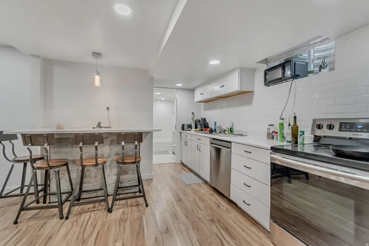 Kitchen with stainless steel appliances, light countertops, white cabinetry, light wood-type flooring, and a breakfast bar area