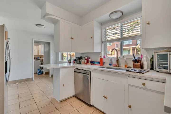 Kitchen with white cabinets, washer / dryer, stainless steel appliances, light tile patterned floors, and decorative backsplash