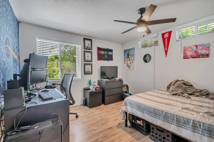 Bedroom featuring an office area, light wood-type flooring, ceiling fan, and a textured ceiling. Two windows