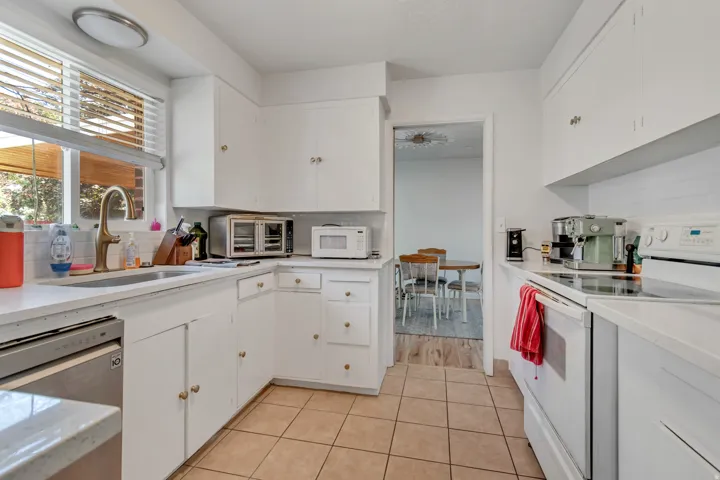 Kitchen with white appliances, white cabinetry, tasteful backsplash, light tile patterned flooring, and light stone counters