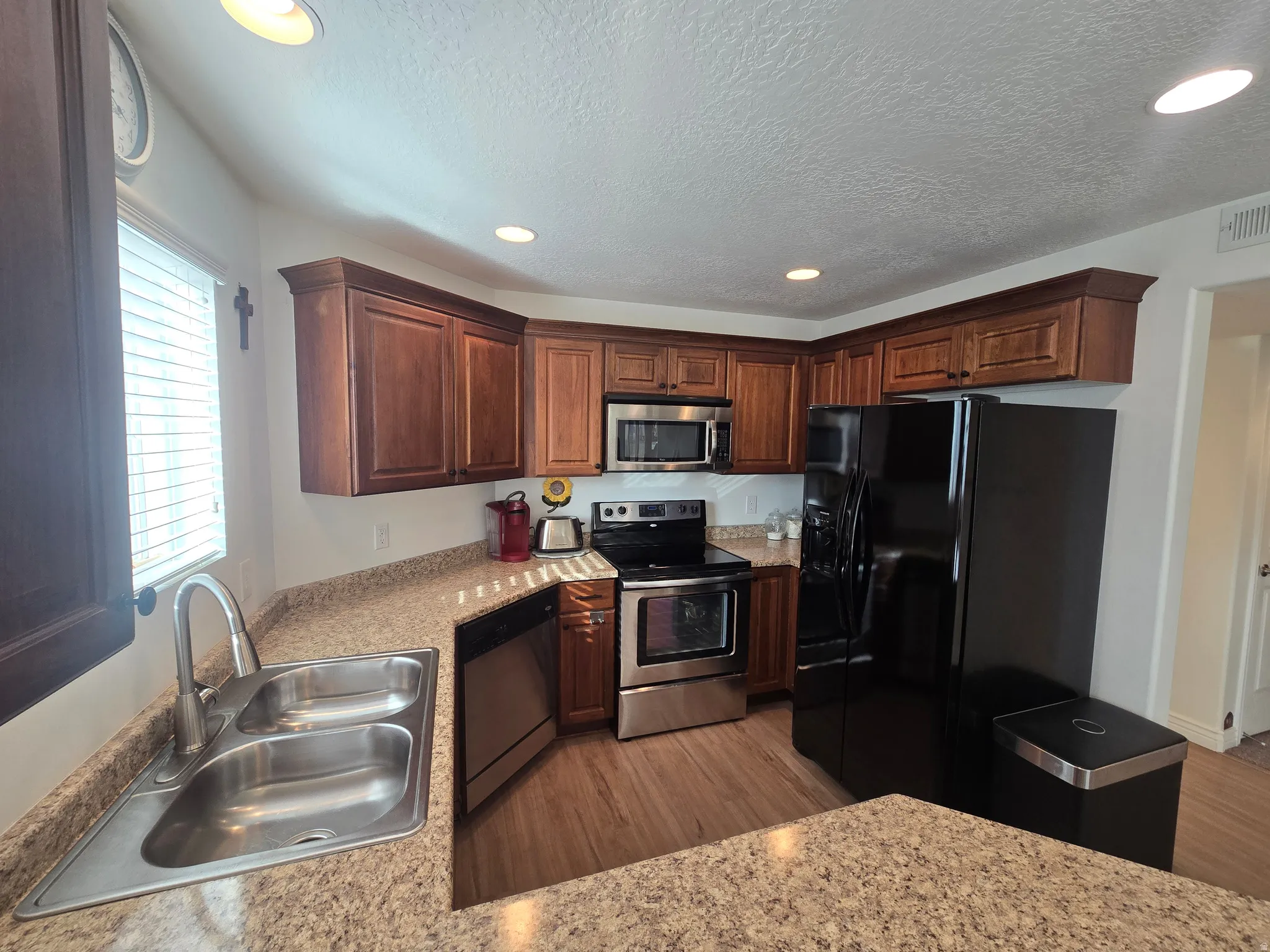 Kitchen featuring stainless steel appliances, recessed lighting, light wood-type flooring, light stone countertops, and a textured ceiling