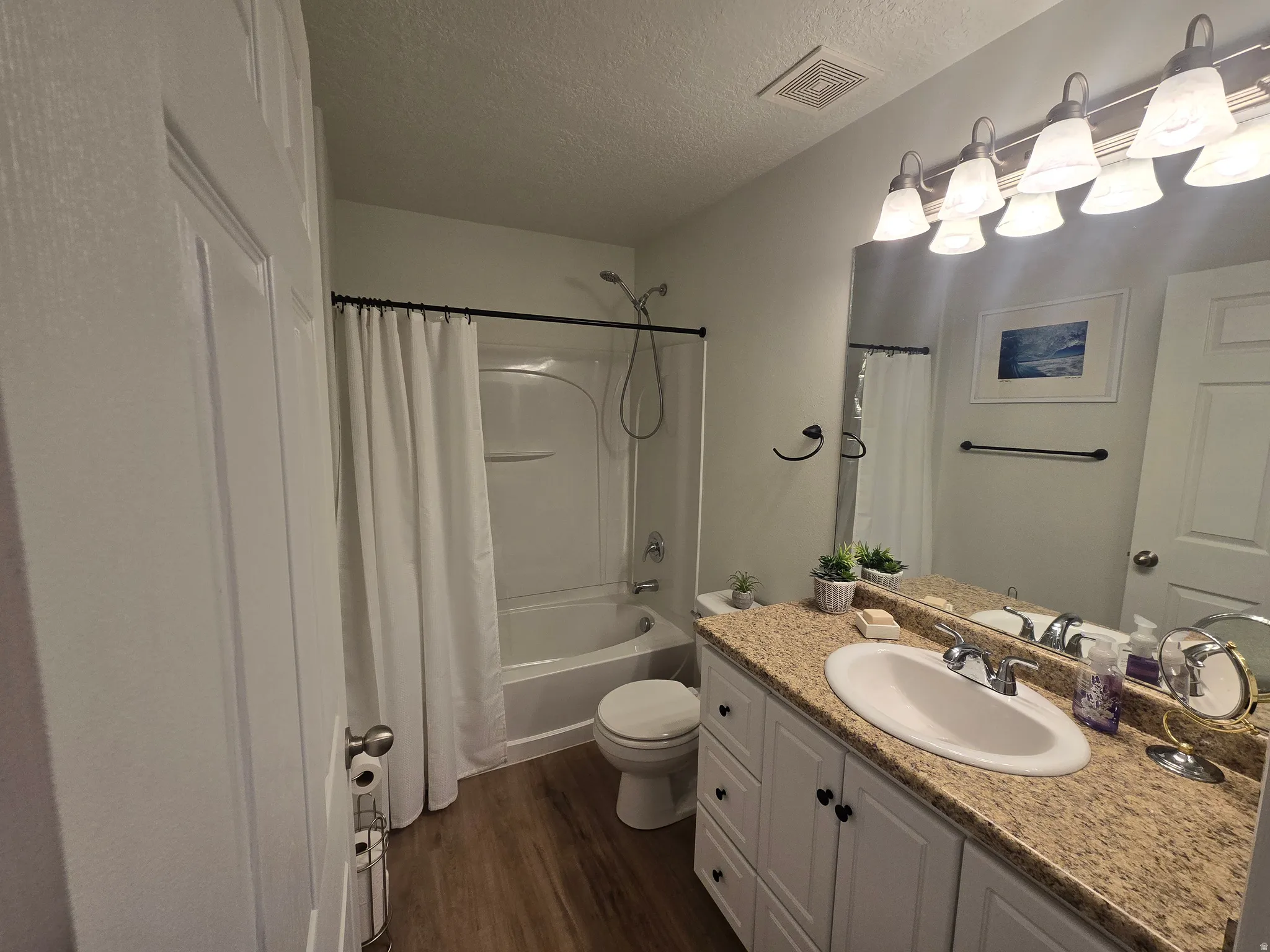 Full bath featuring vanity, a textured ceiling, dark wood finished floors, and shower / bath combination with curtain