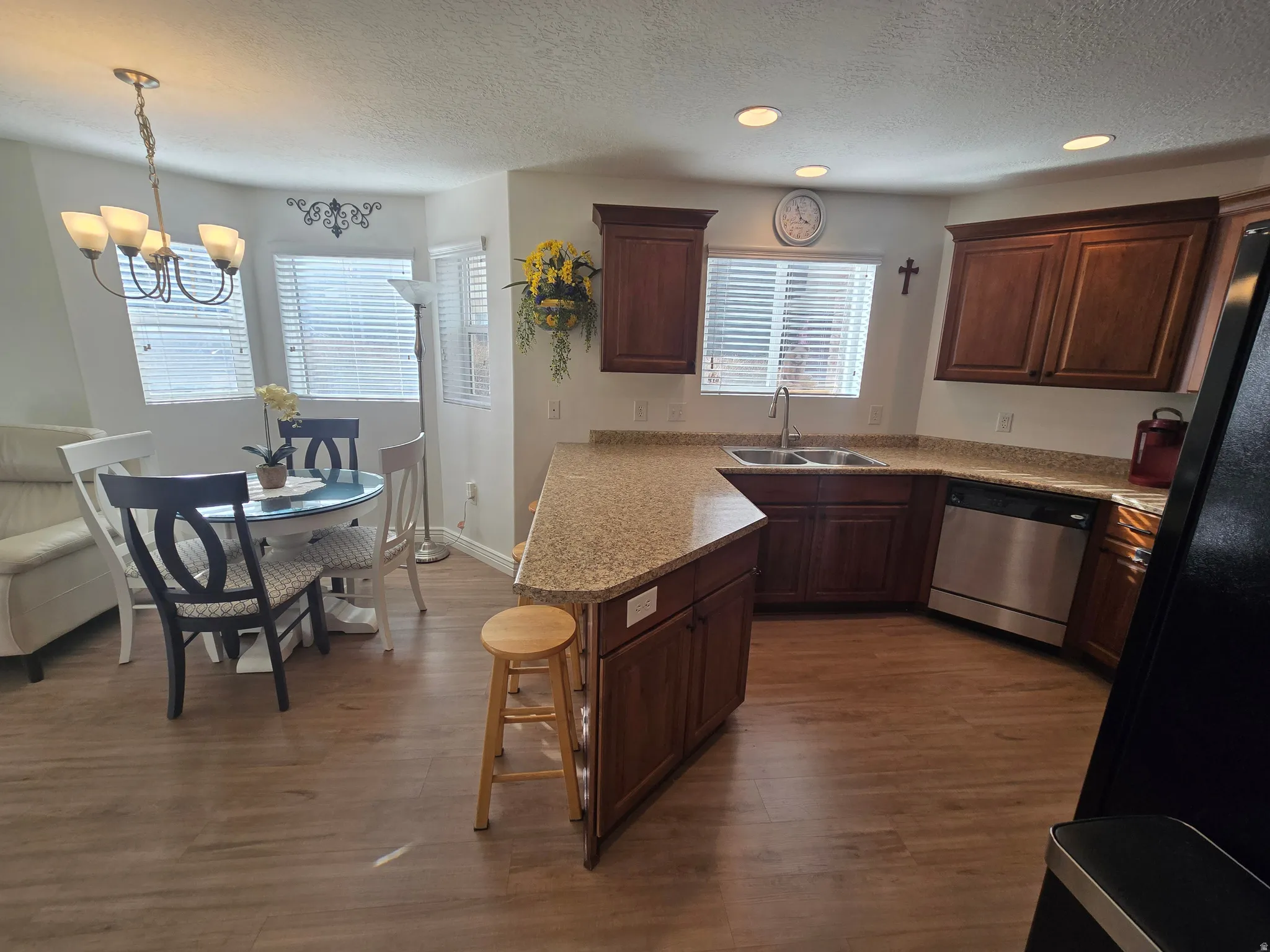 Kitchen featuring a peninsula, a textured ceiling, dishwasher, a breakfast bar, and dark wood finished floors