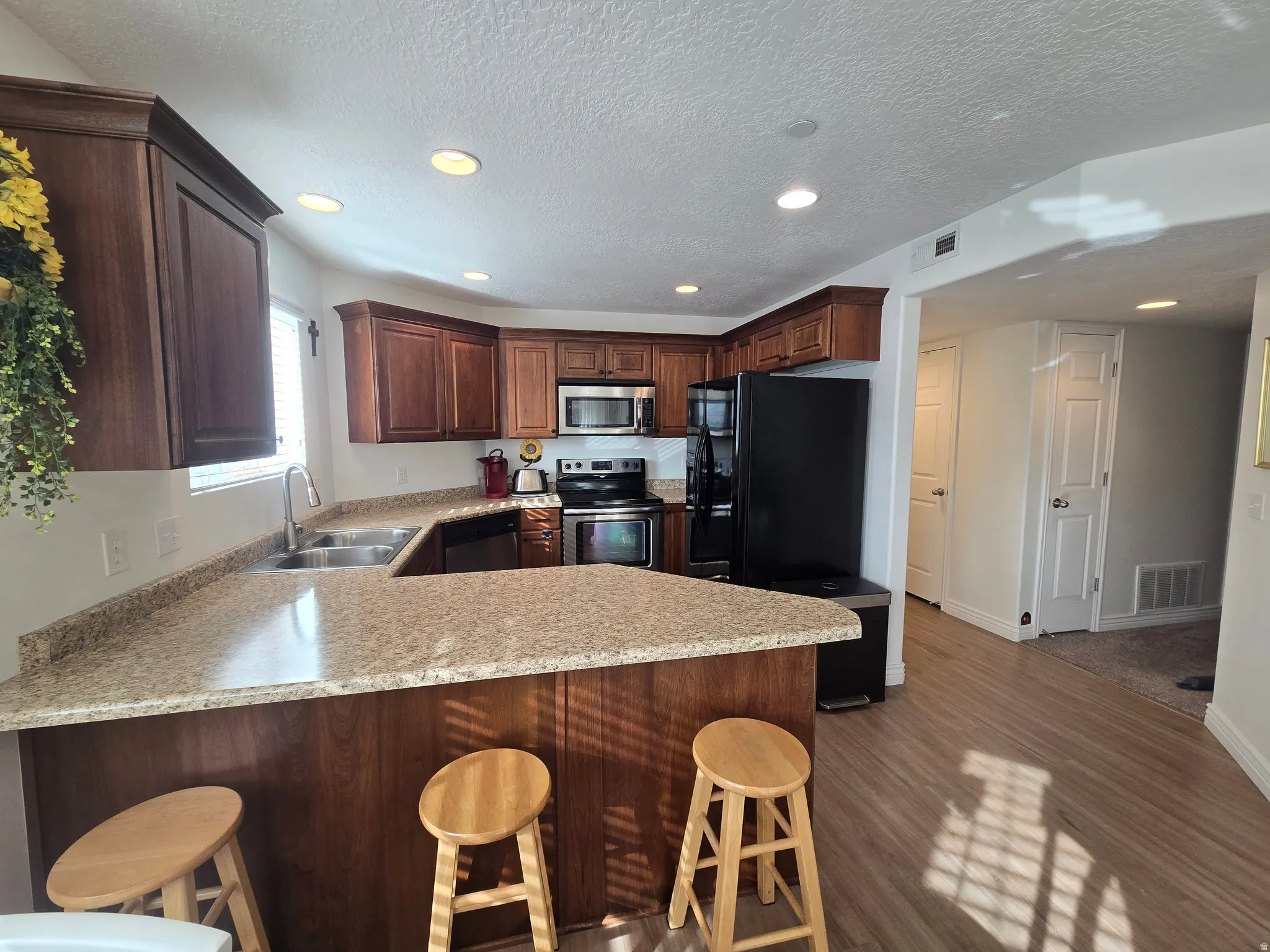 Kitchen with a kitchen breakfast bar, a peninsula, stainless steel appliances, recessed lighting, and dark wood finished floors