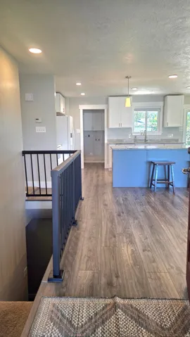 Wood-finish flooring throughout, kitchen with white cabinetry and light-toned countertops, recessed lighting, and a kitchen island with pendant lighting
