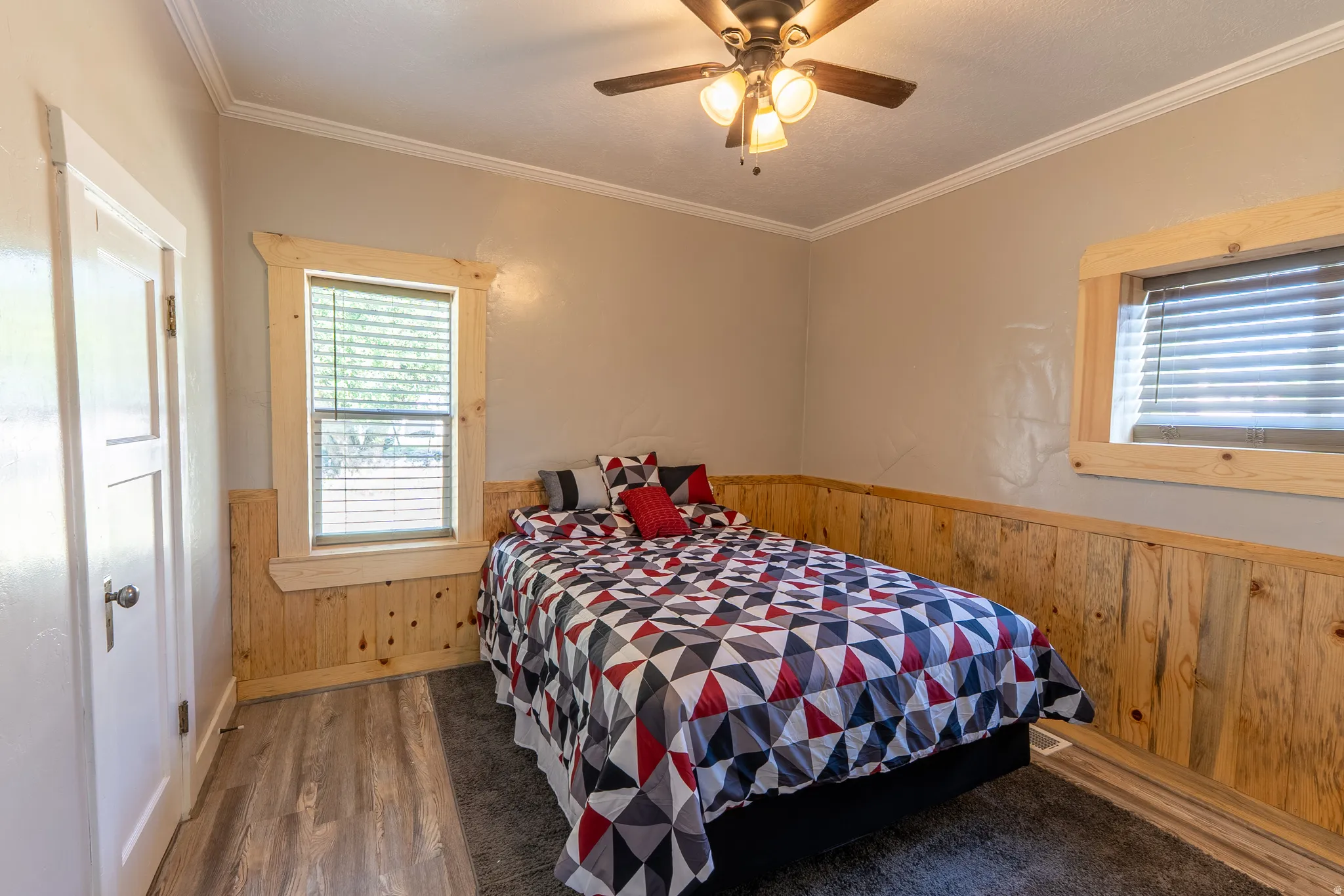 Bedroom with wooden walls, wainscoting, dark wood finished floors, ceiling fan, and crown molding