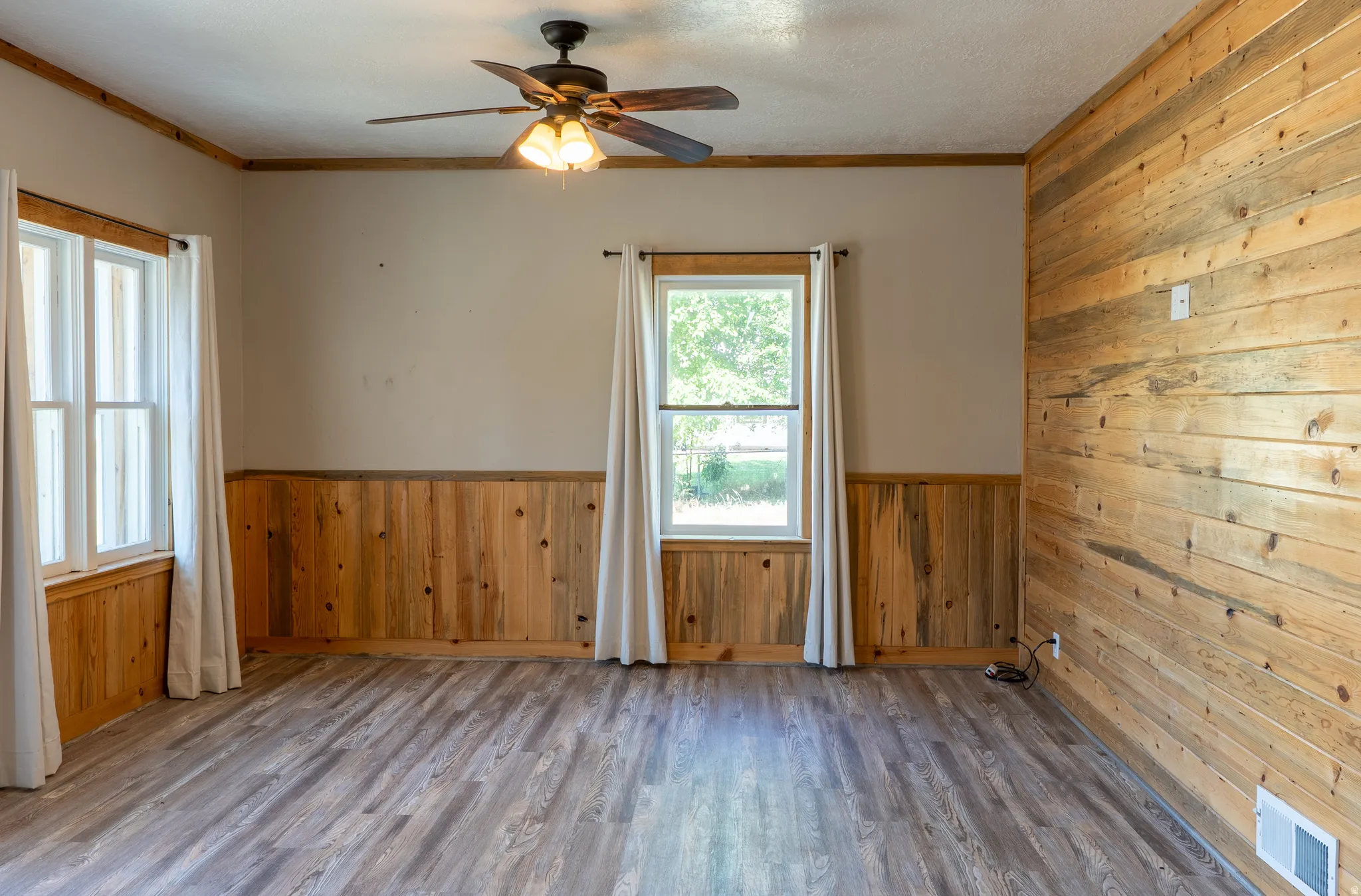 Spare room featuring wooden walls, wainscoting, wood finished floors, ceiling fan, and ornamental molding