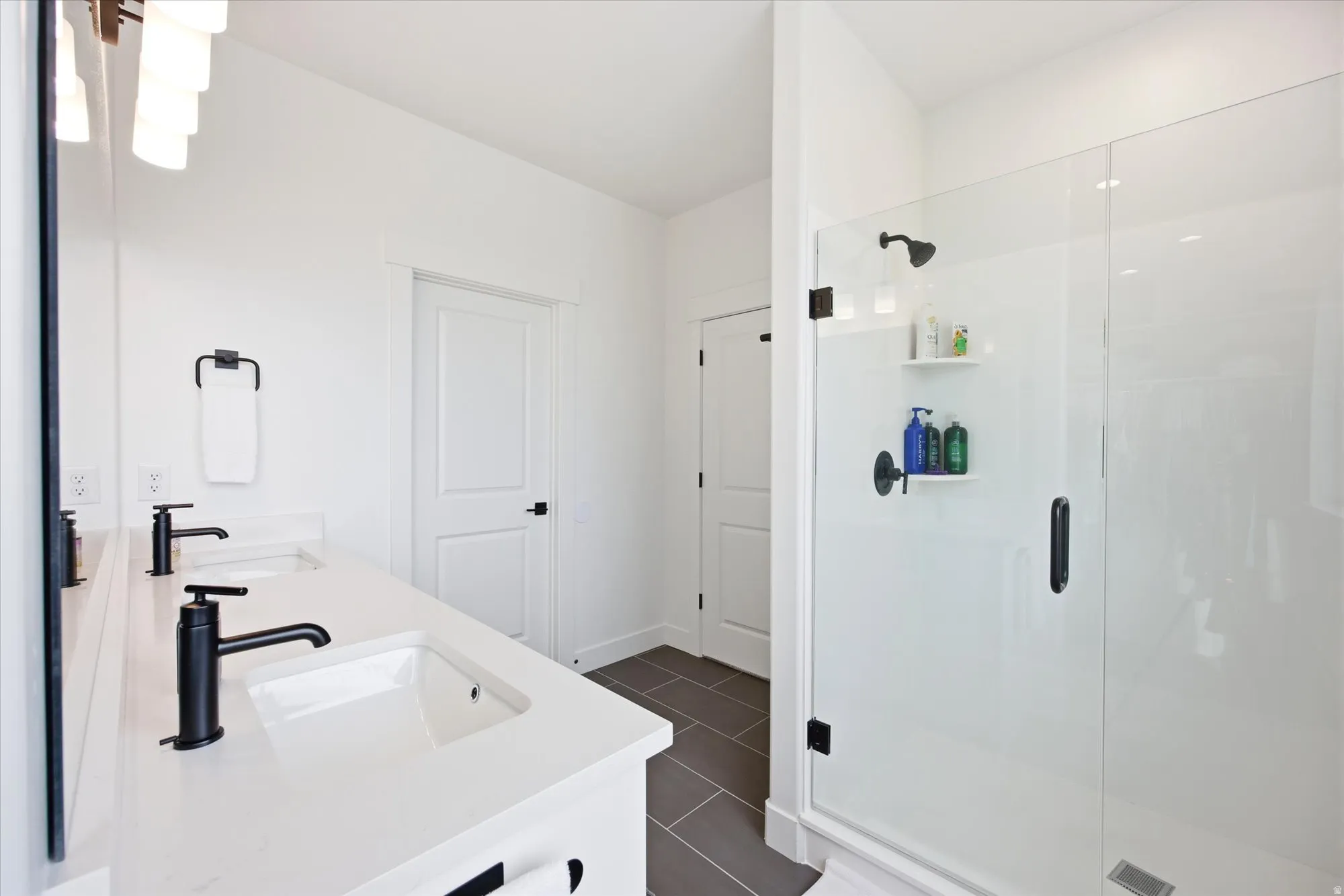 Full bathroom with double vanity, a stall shower, and dark tile patterned flooring
