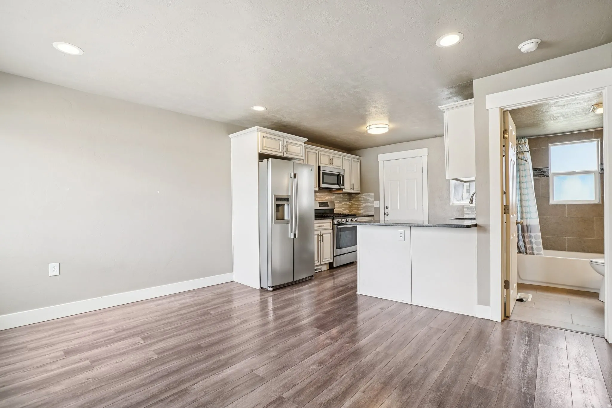 Kitchen with stainless steel appliances, tasteful backsplash, dark wood-type flooring, white cabinets, and a peninsula