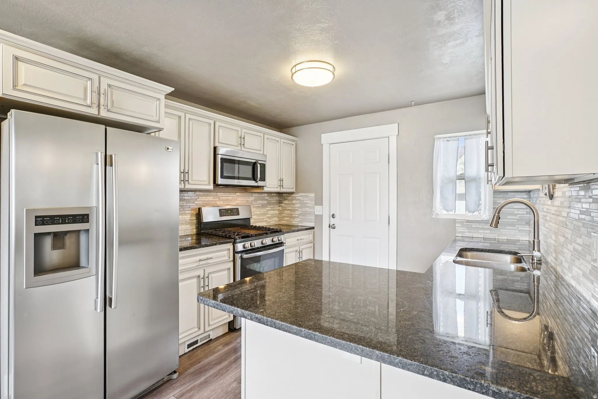 Kitchen with stainless steel appliances, light wood-style flooring, dark stone counters, and white cabinetry