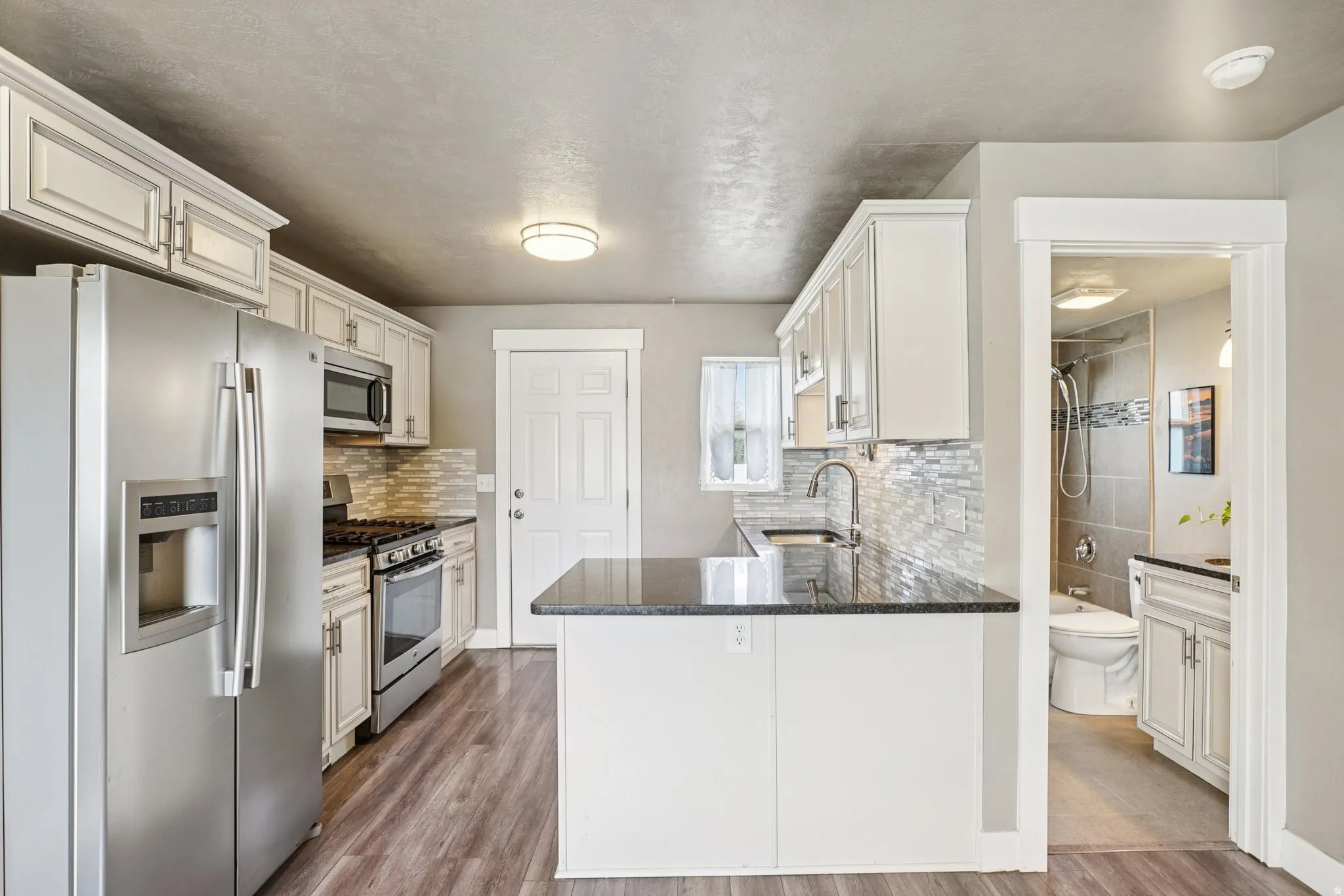 Kitchen featuring stainless steel appliances, dark stone counters, dark wood-type flooring, and white cabinets