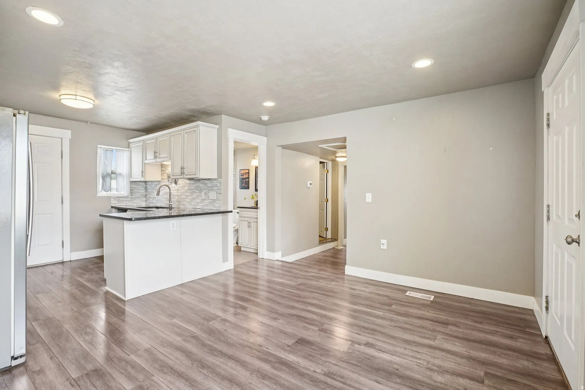 Kitchen featuring white cabinets, light wood-style flooring, freestanding refrigerator, decorative backsplash, and recessed lighting