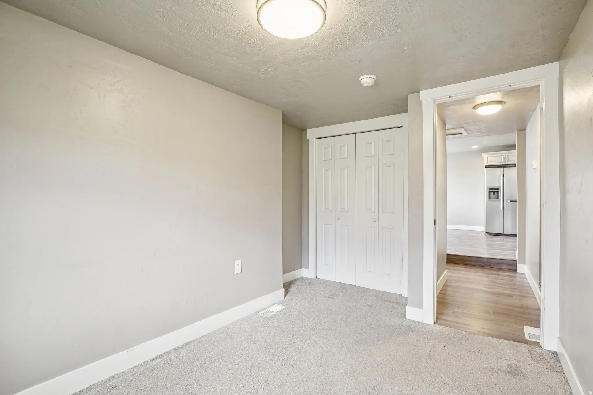 Unfurnished bedroom with stainless steel fridge, light colored carpet, a closet, and a textured ceiling
