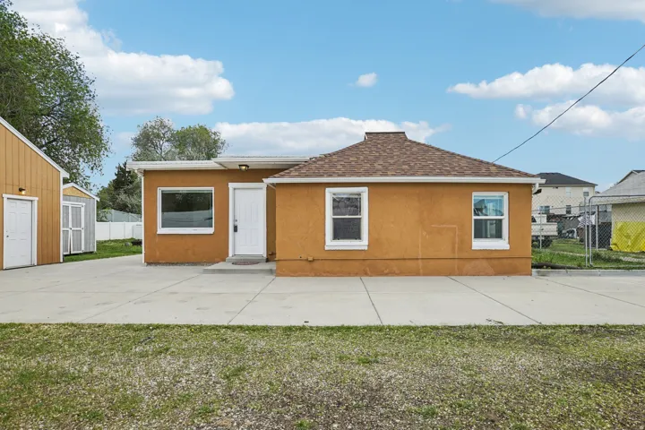 View of front of home with a shingled roof, stucco siding, a storage unit, and a patio