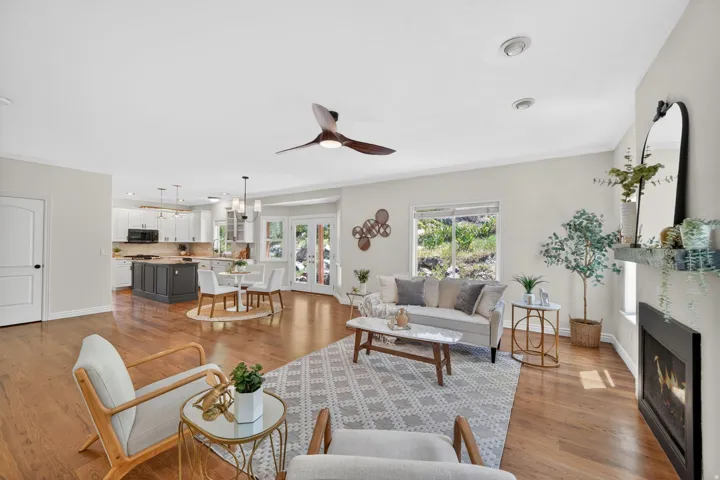 Open-concept living area featuring wood-finish flooring, a contemporary ceiling fan, and a fireplace with a mantel