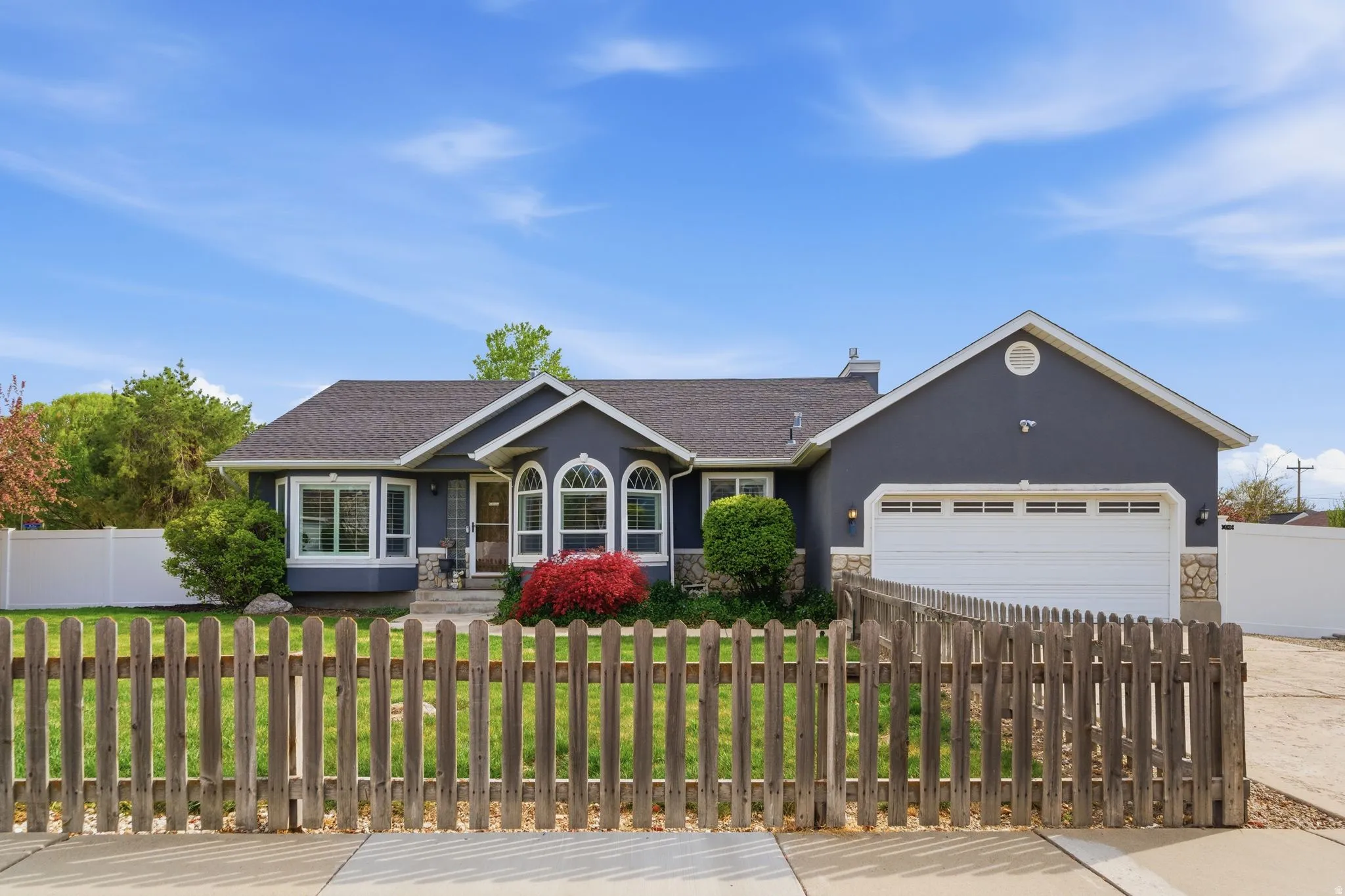 Ranch-style house featuring stone siding, stucco siding, a fenced front yard, a garage, and driveway