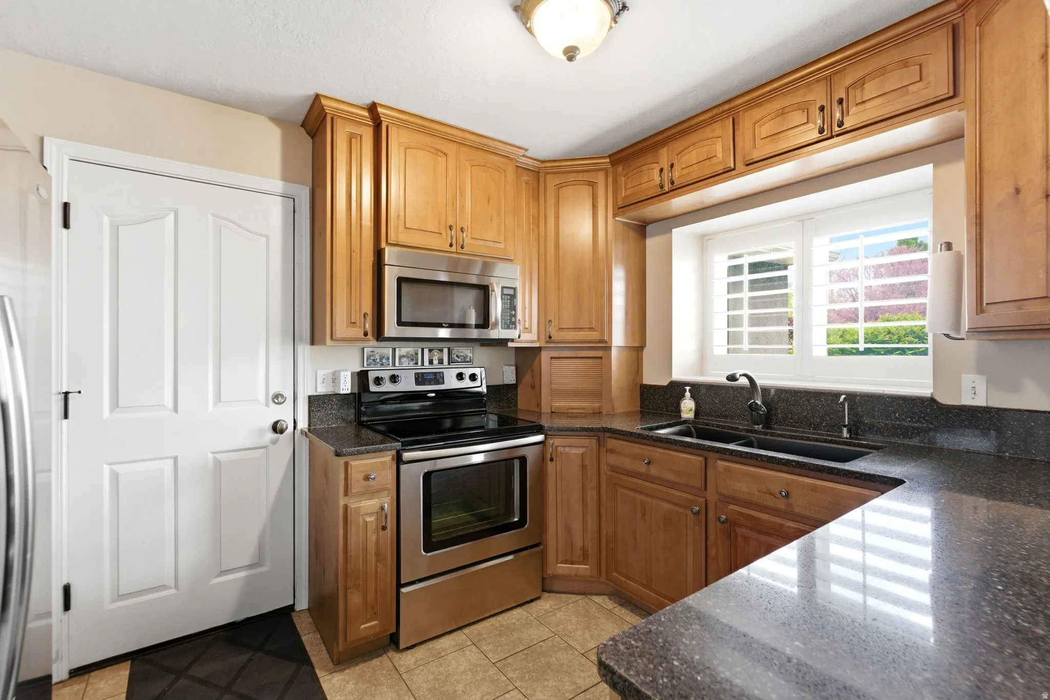 Kitchen with stainless steel appliances, dark stone counters, wood finish cabinets, and light tile patterned floors