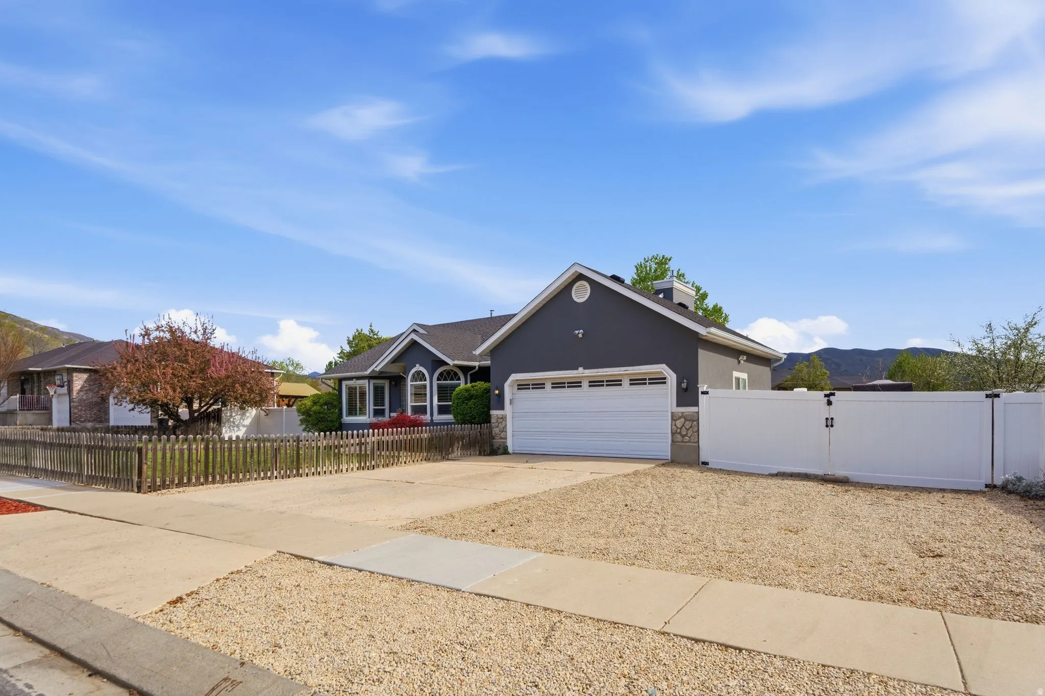 Ranch-style home featuring a fenced front yard, a gate, stone siding, and driveway