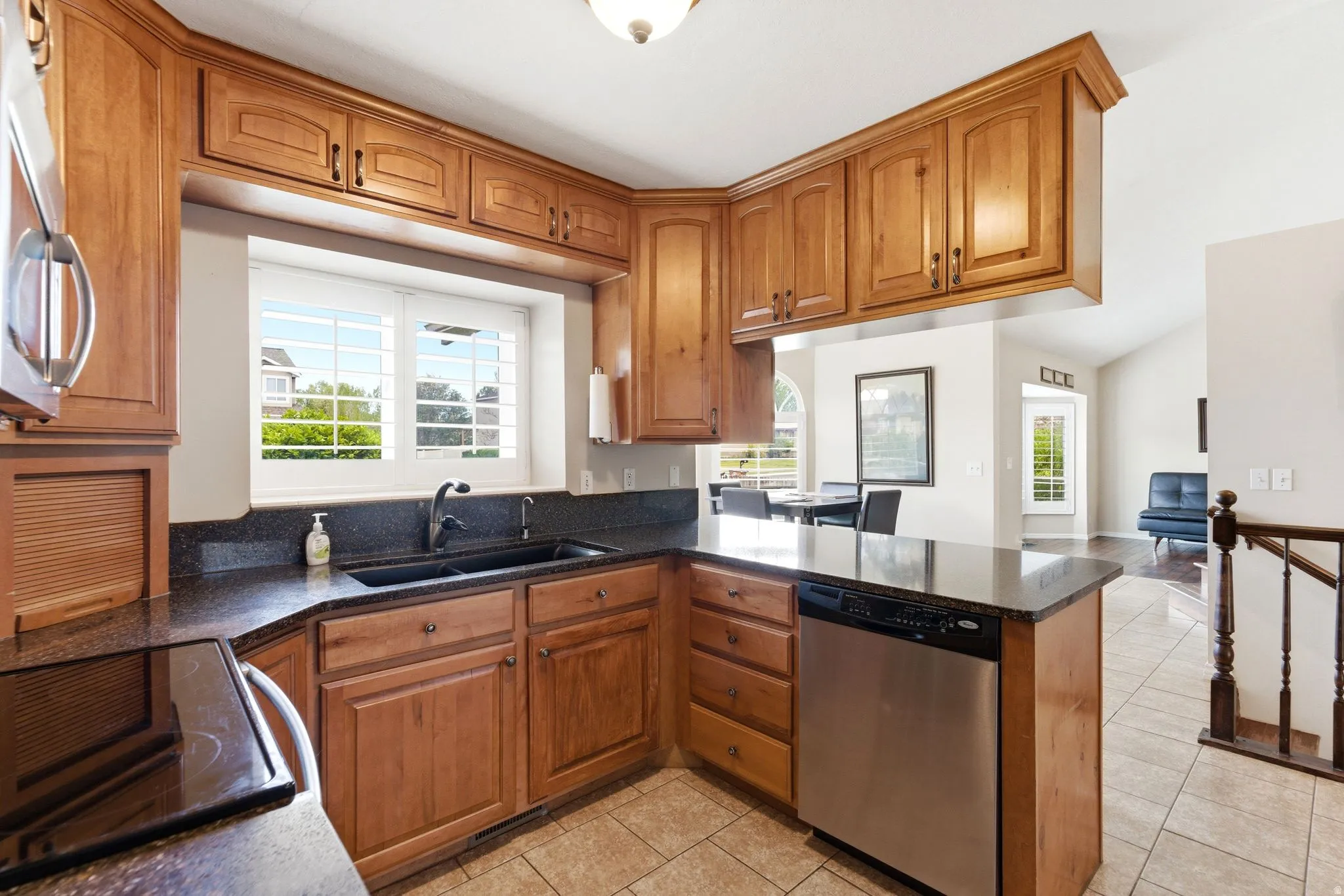 Kitchen with wood finish cabinets, stainless steel appliances, dark stone countertops, light tile patterned flooring, and a peninsula
