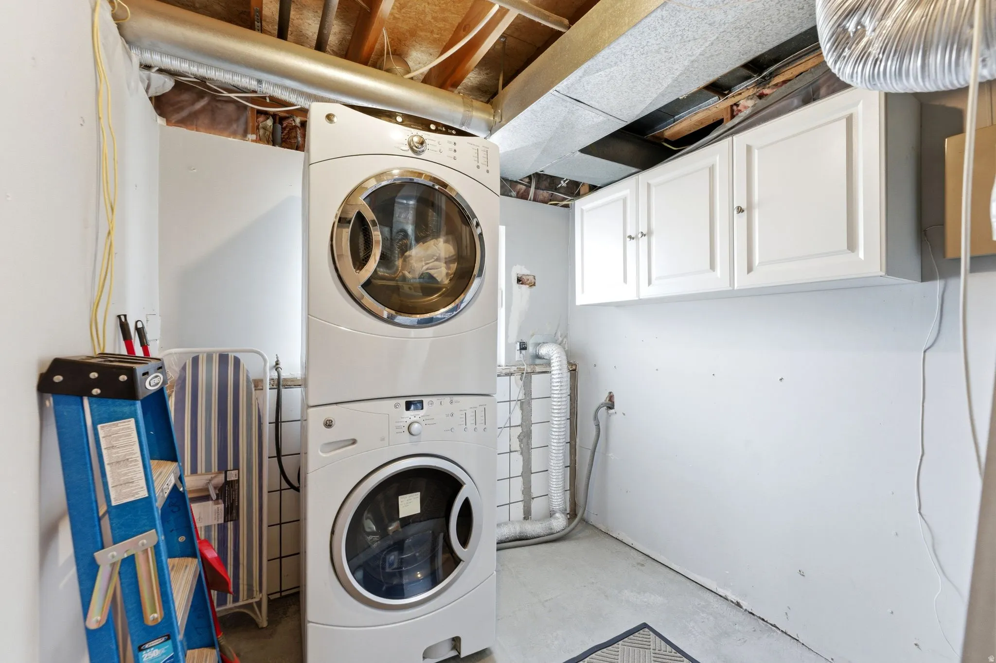 Laundry room with concrete floors, stacked washing machine and dryer, and cabinet space