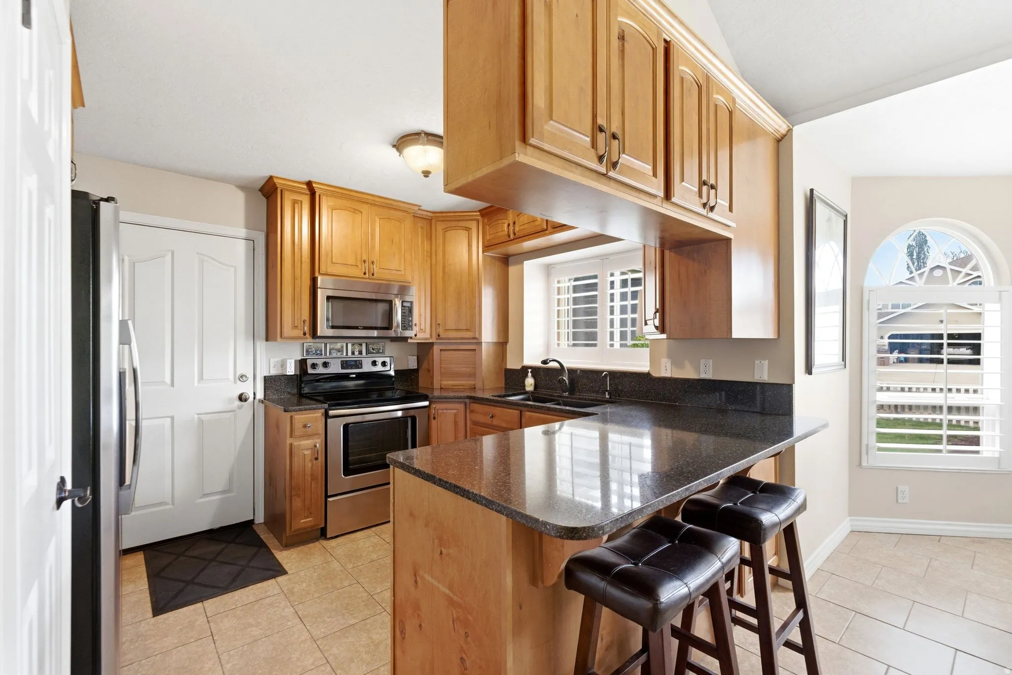Kitchen with a kitchen breakfast bar, stainless steel appliances, a peninsula, light tile patterned floors, and wood finish cabinetry