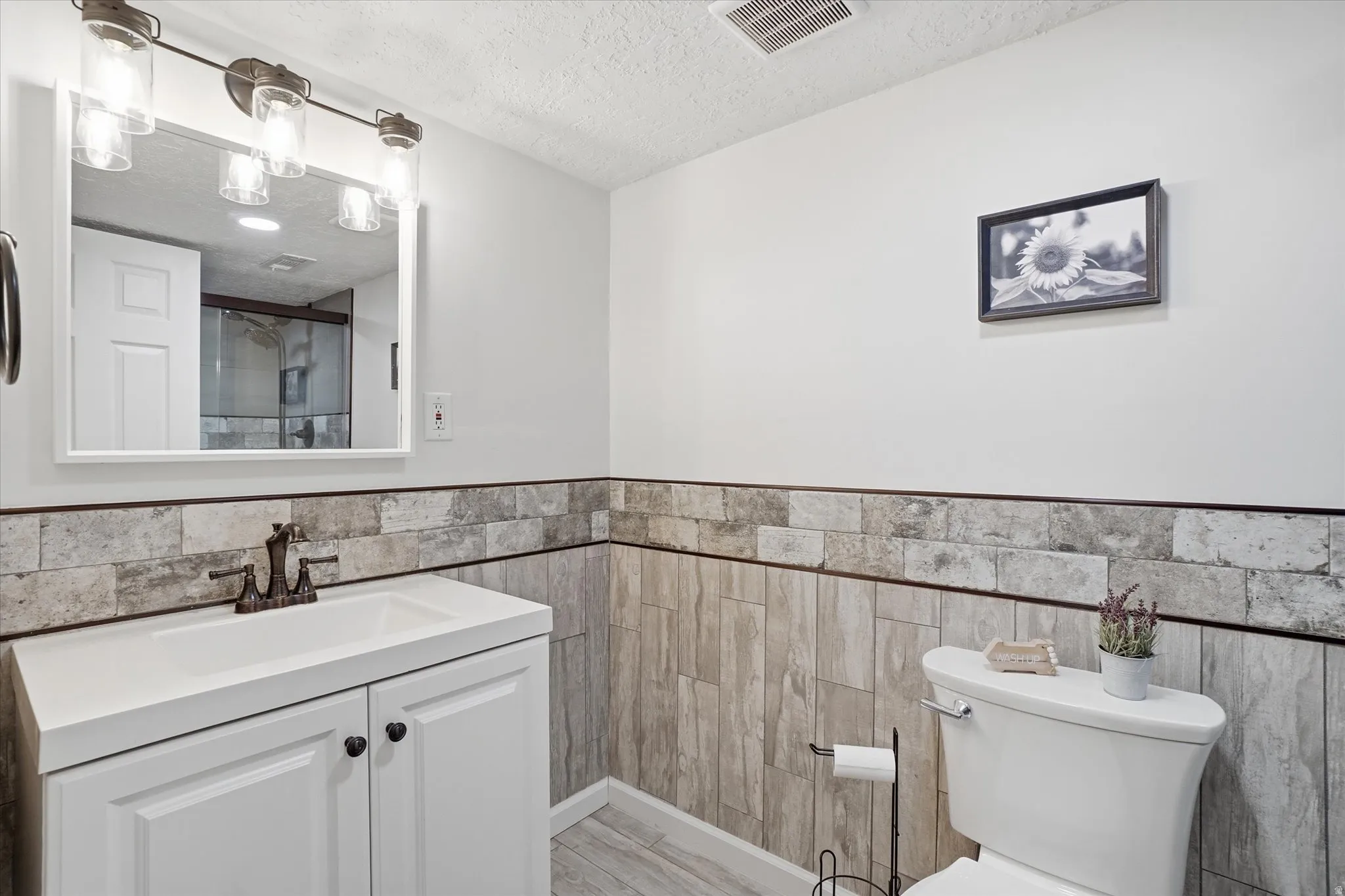 Bathroom with vanity, a textured ceiling, wainscoting, tile walls, and a shower with shower door