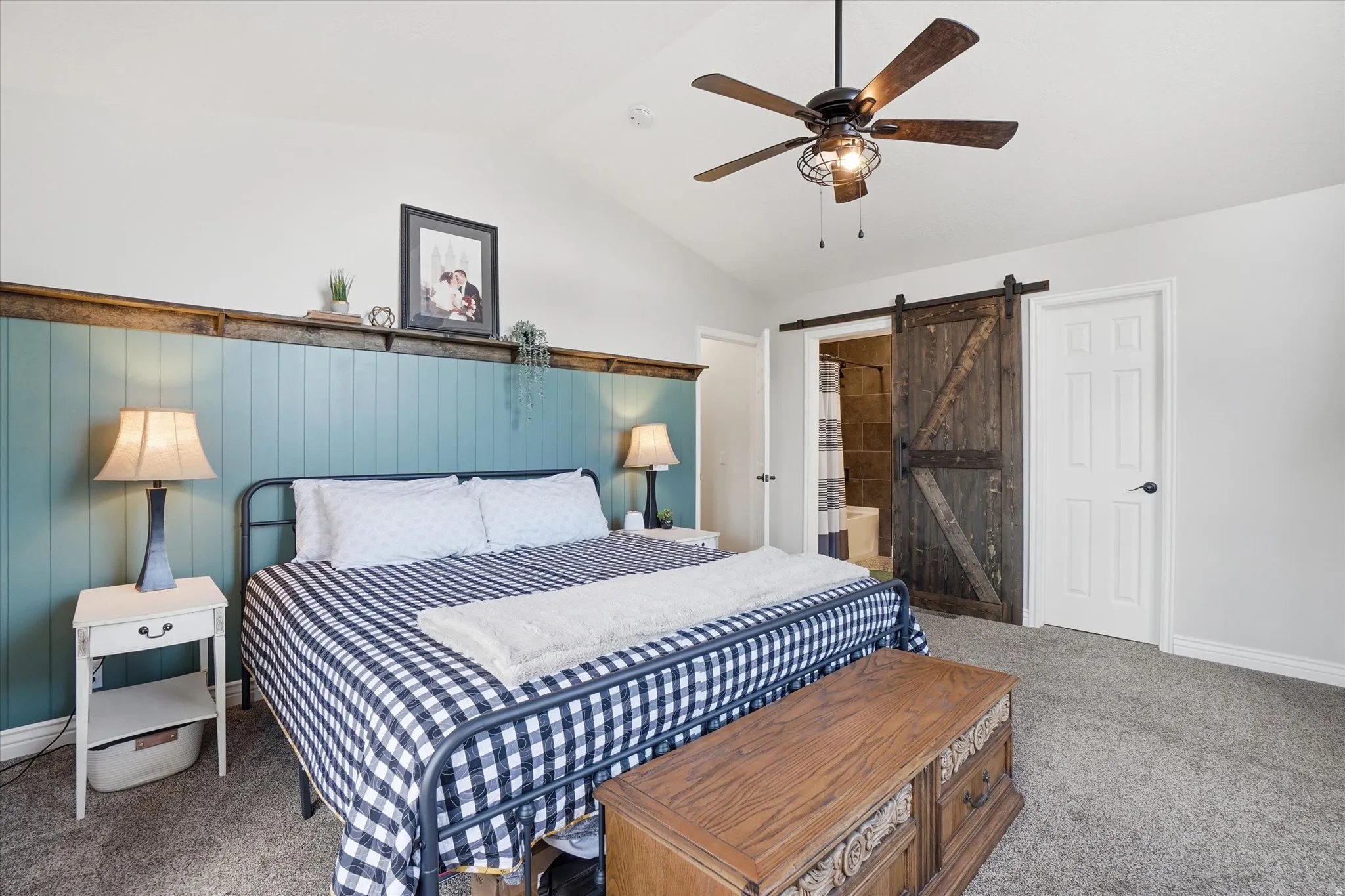 Bedroom featuring a barn door, carpet floors, vaulted ceiling, ensuite bath, and a ceiling fan
