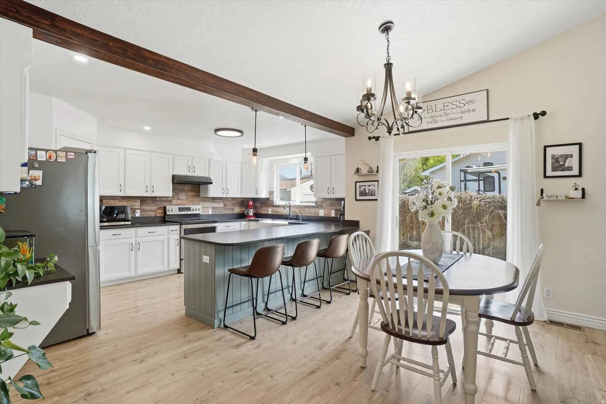 Two tone kitchen with dark countertops, stainless steel appliances, hanging lights, a breakfast bar area, and a peninsula