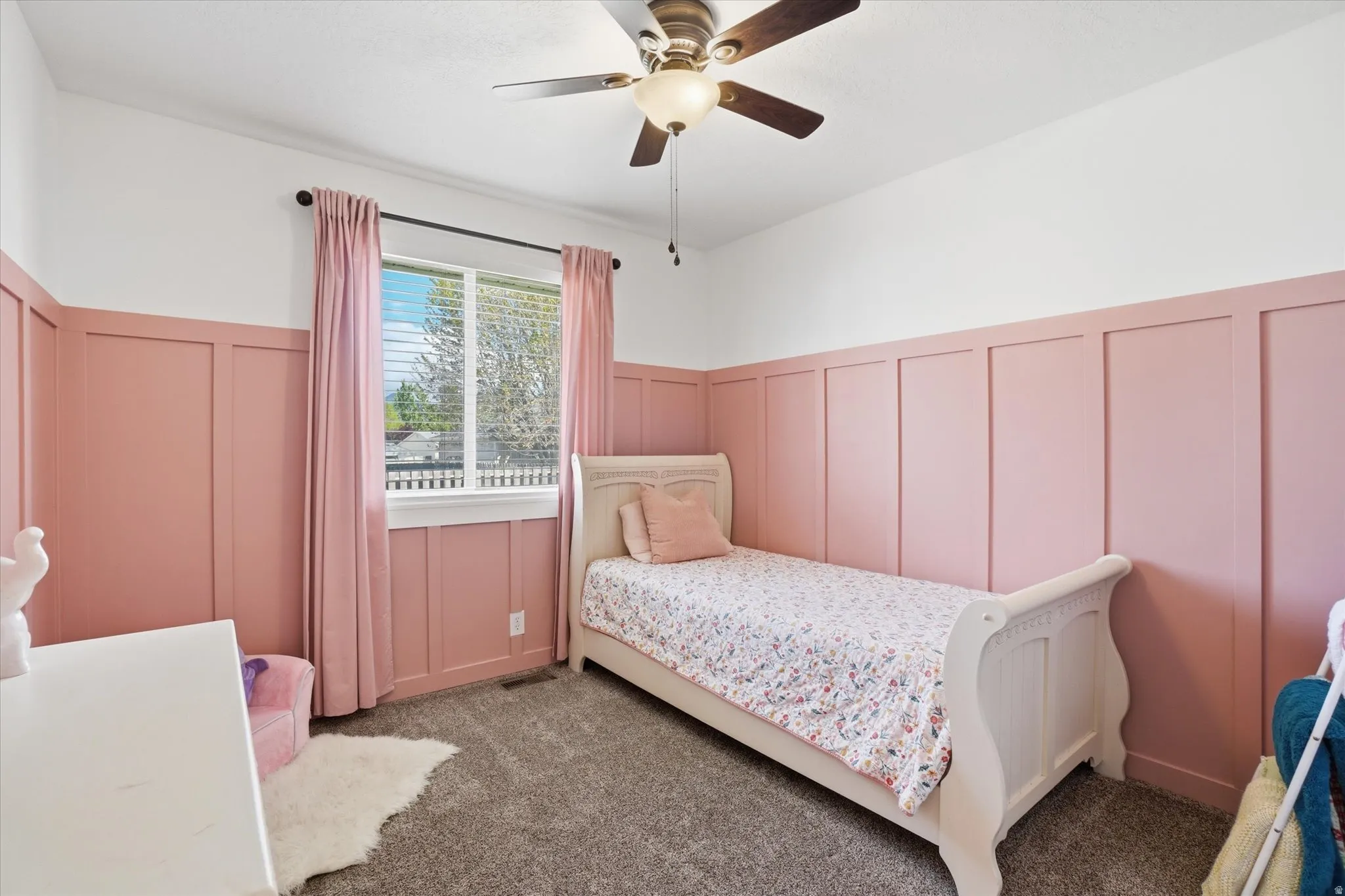 Carpeted bedroom with a decorative wall, wainscoting, and ceiling fan