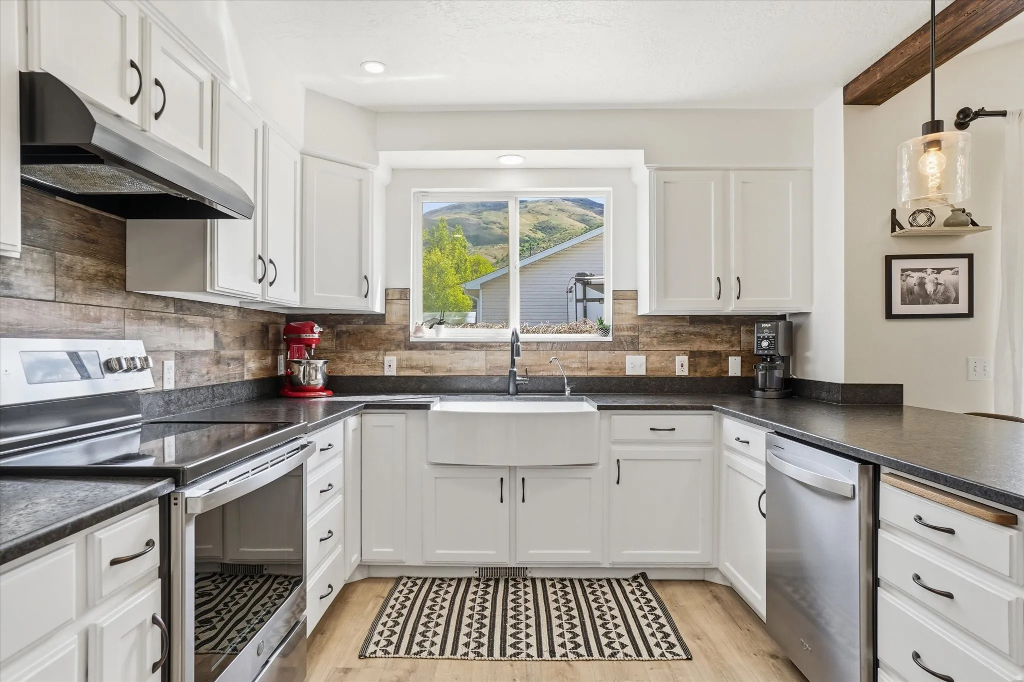 Kitchen featuring stainless steel appliances, white cabinetry, dark countertops, and light wood-type flooring
