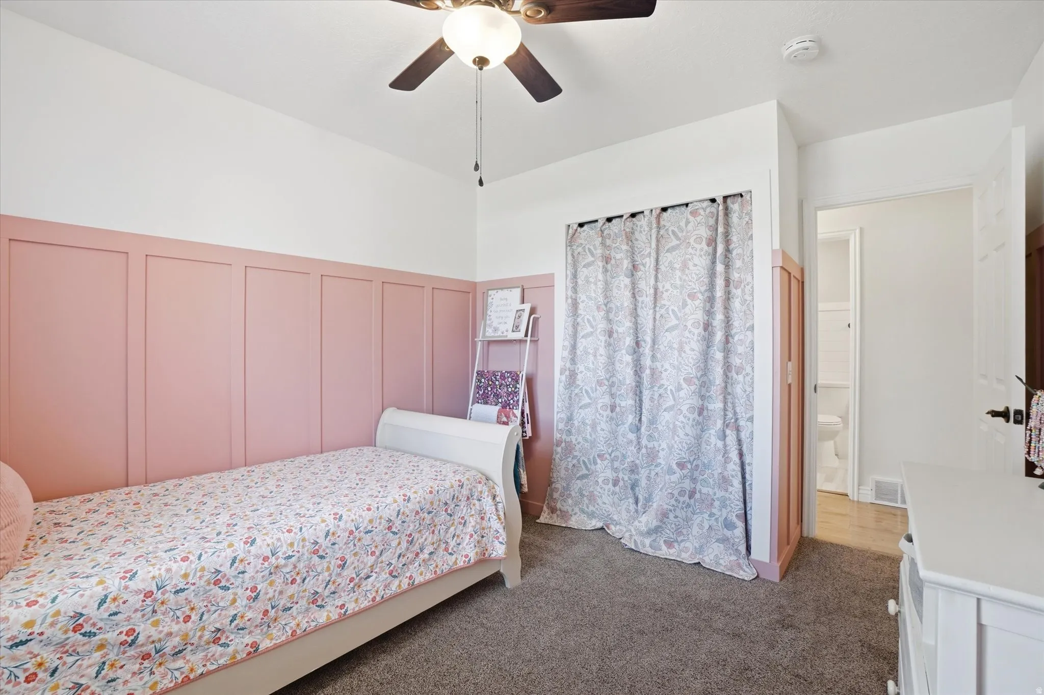Bedroom featuring a decorative wall, dark colored carpet, a ceiling fan, and wainscoting