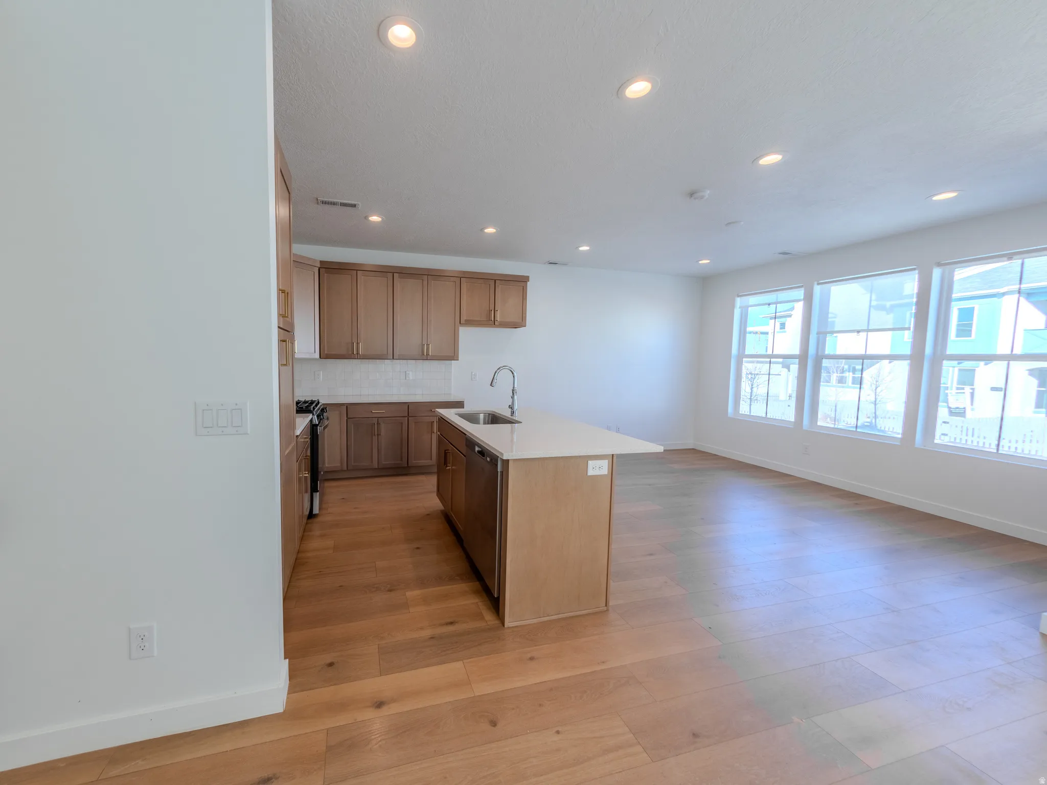 Kitchen with a center island with sink, light wood-type flooring, recessed lighting, tasteful backsplash, and range with gas stovetop