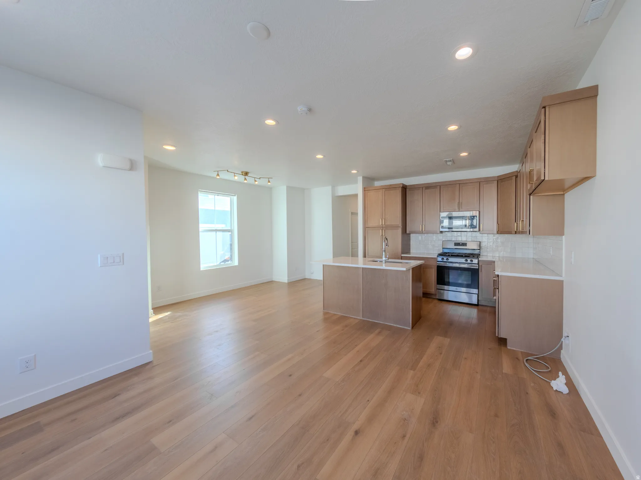Kitchen with stainless steel appliances, a center island with sink, light wood-type flooring, tasteful backsplash, and open floor plan