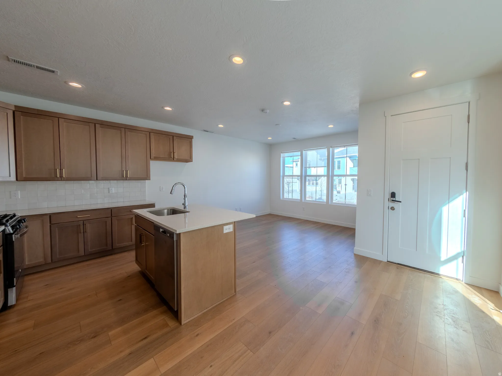 Kitchen with a center island with sink, decorative backsplash, light wood finished floors, recessed lighting, and open floor plan