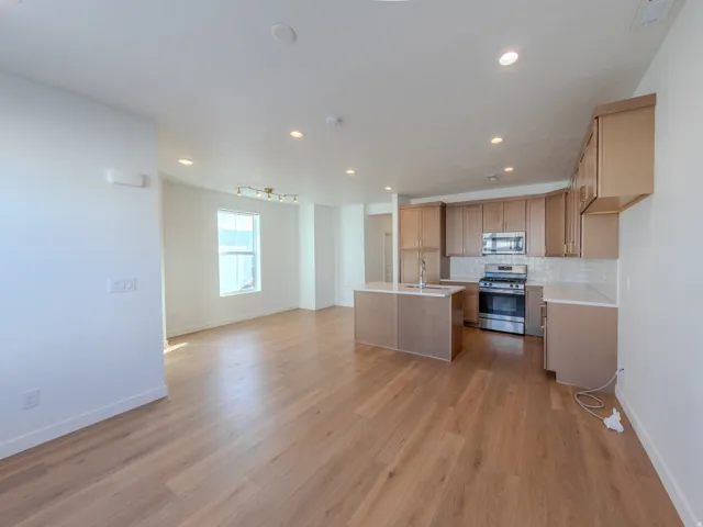 Kitchen with stainless steel appliances, a center island with sink, light wood-type flooring, tasteful backsplash, and open floor plan