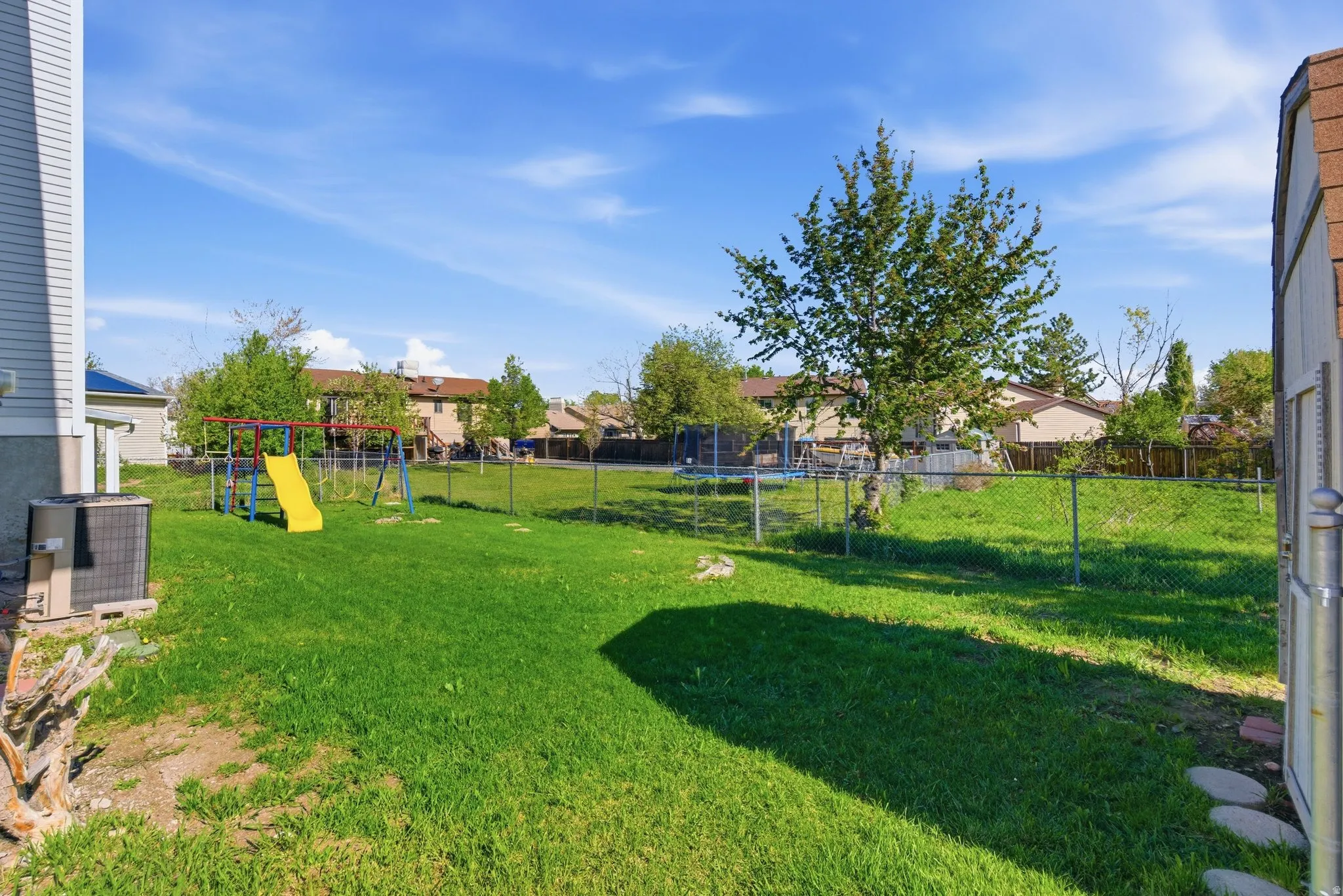 Fenced backyard featuring a trampoline, a residential view, and a playground