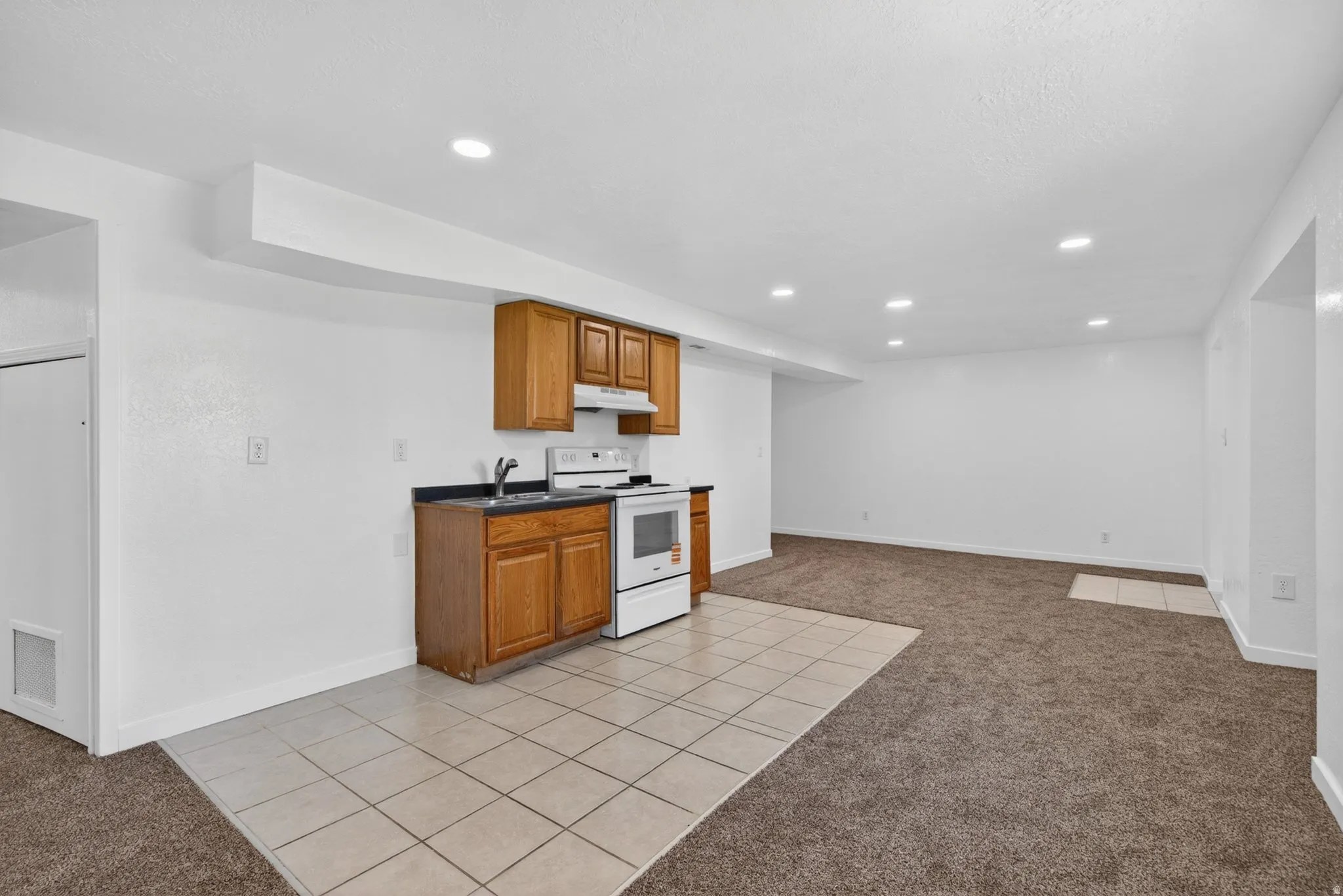 Kitchen with light carpet, light tile patterned flooring, dark countertops, wood finish cabinets, and white electric range