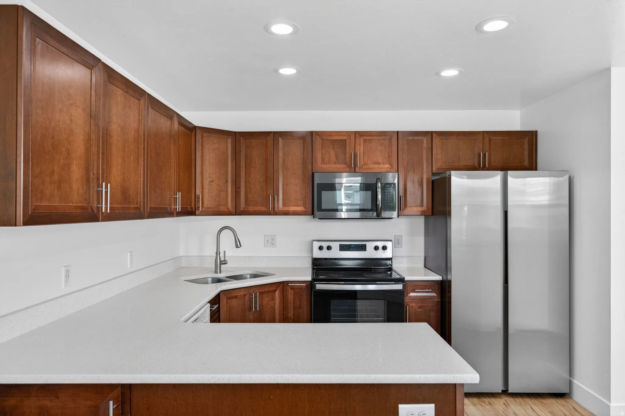 Kitchen with stainless steel appliances, light stone counters, a peninsula, recessed lighting, and light wood-style flooring