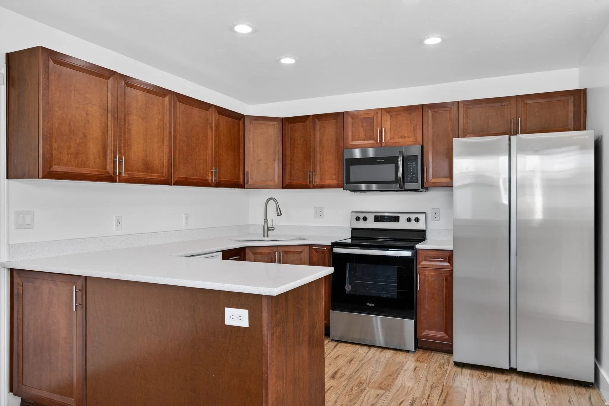 Kitchen featuring stainless steel appliances, a peninsula, light wood finished floors, recessed lighting, and wood finish cabinetry