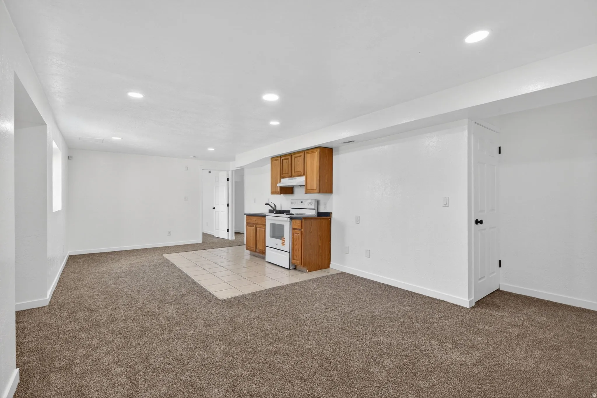 Kitchen featuring dark countertops, electric stove, wood finish cabinets, open floor plan, and light carpet