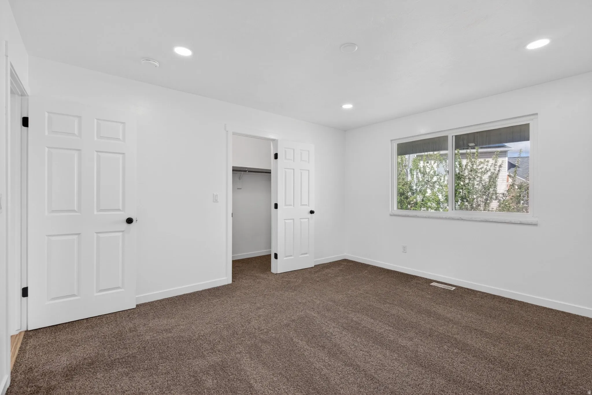 Unfurnished bedroom featuring a spacious closet, dark colored carpet, and recessed lighting