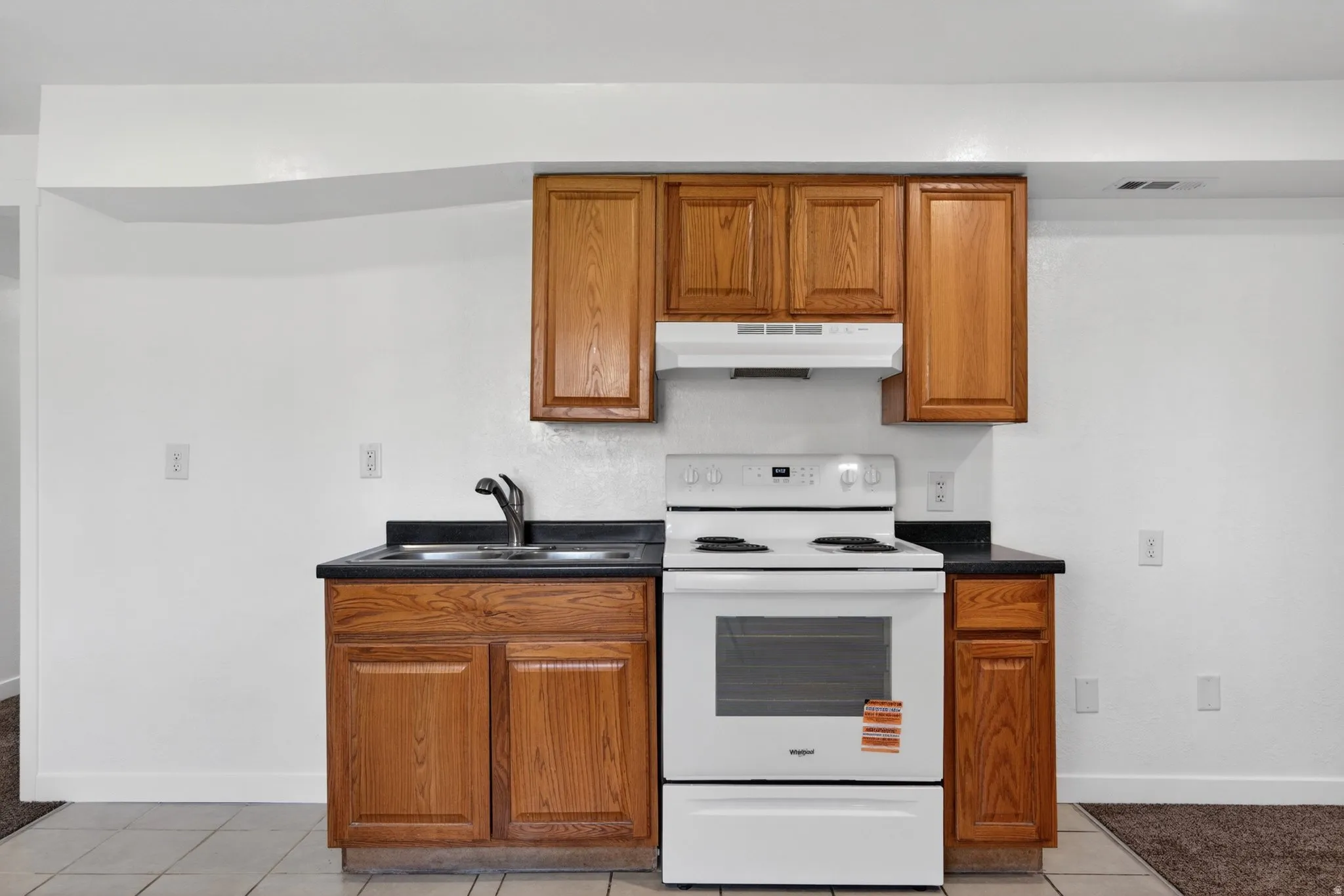 Kitchen featuring electric stove, dark countertops, wood finish cabinetry, and light tile patterned flooring