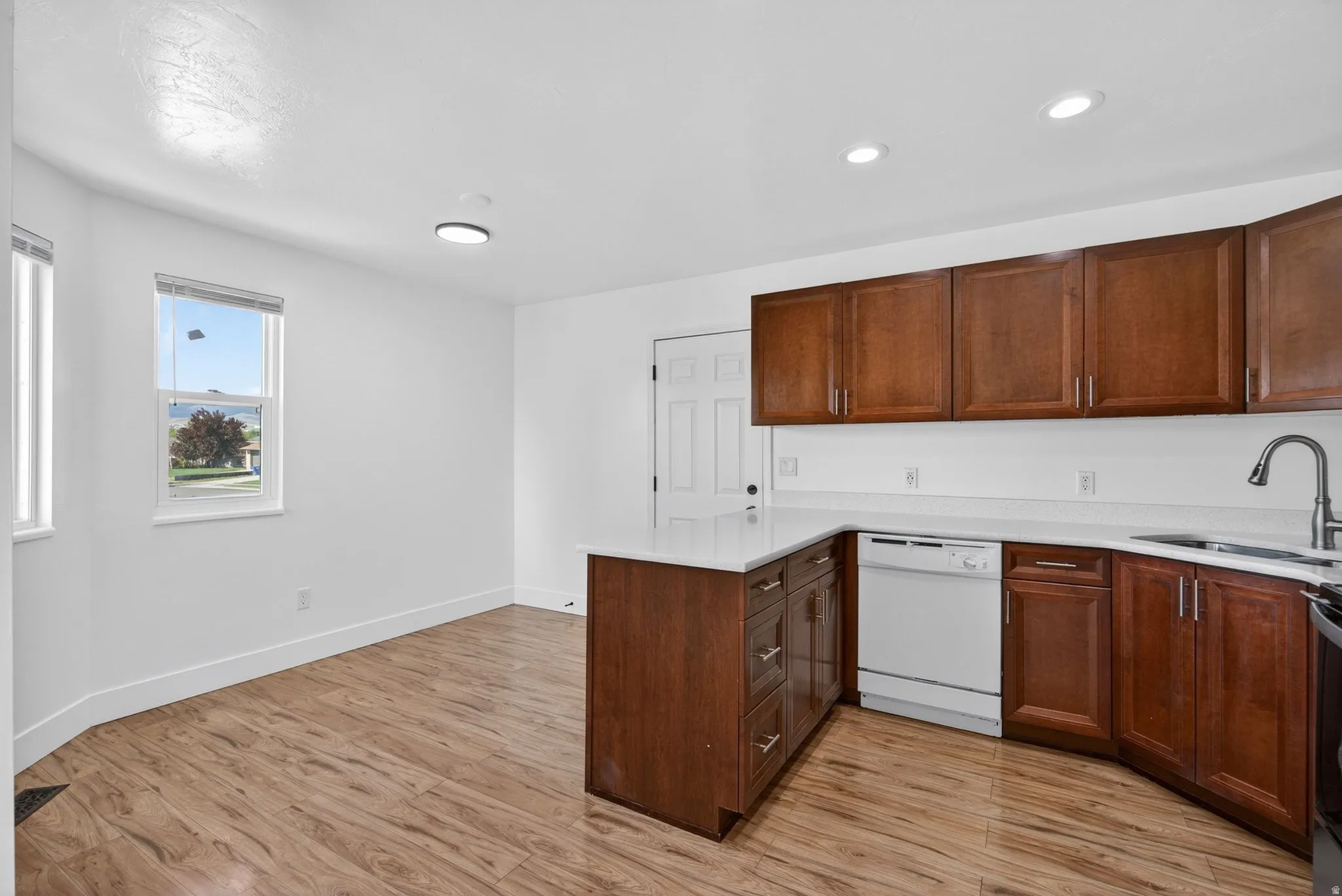 Kitchen with a peninsula, dishwasher, light wood-style floors, and light stone countertops