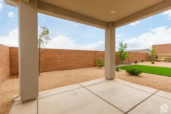 Covered patio with concrete flooring, gravel landscaping, block wall perimeter, and artificial turf