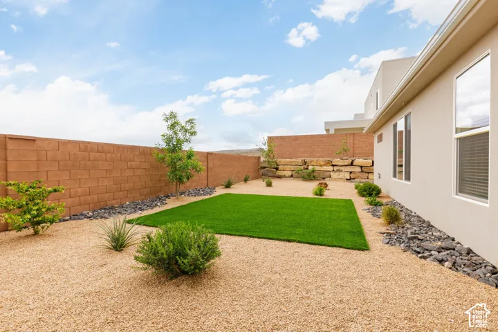 Landscaped backyard featuring a synthetic lawn area, gravel ground cover, a block privacy wall, and planted shrubs