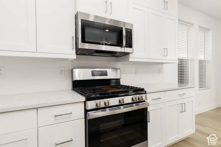 White shaker cabinetry, stainless steel oven/range, integrated microwave, light countertops, and white subway tile backsplash