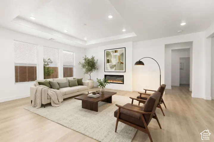 Recessed lighting, wood-finish flooring, an electric fireplace, multiple windows with blinds, and tray ceiling detailing